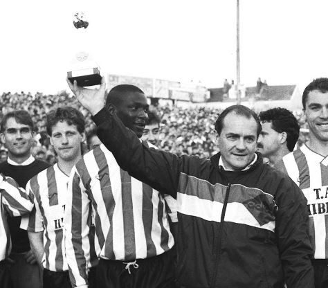 Exeter City Manager, Terry Cooper holds Fourth Division championship trophy, 1990-1 Black and white image of football team and coach celebrating with trophy | Image courtesy of the Grecian Archive