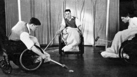 Black and white photo of three men playing a wheelchair sport