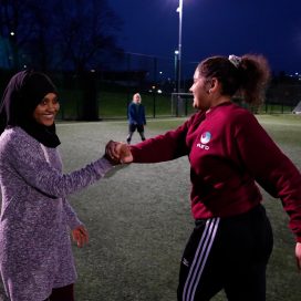 Two young women shake hands on a football pitch