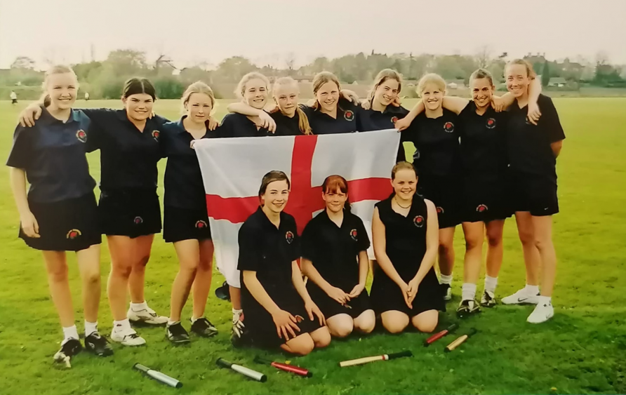 Team photo, girls in black uniforms, holding St Georges flag. | Rounders England