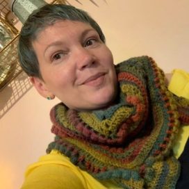 Head and shoulders shot of Debbie Cooper wearing a yellow jumper and chunky kniyyed scarf.
