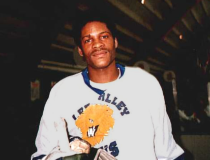 Head and shoulders of a black man wearing a Lee Valley Lions sweatshirt, with lion to centre. Can be seen holding top of ice hockey stick. | Courtesy of Ice Hockey UK Media.