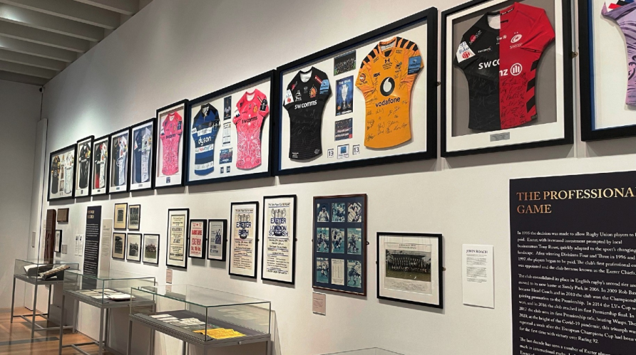 White gallery space with display cases and walled frames showing rugby shirts, team photos and other memorabilia | Courtesy of South West Heritage Trust