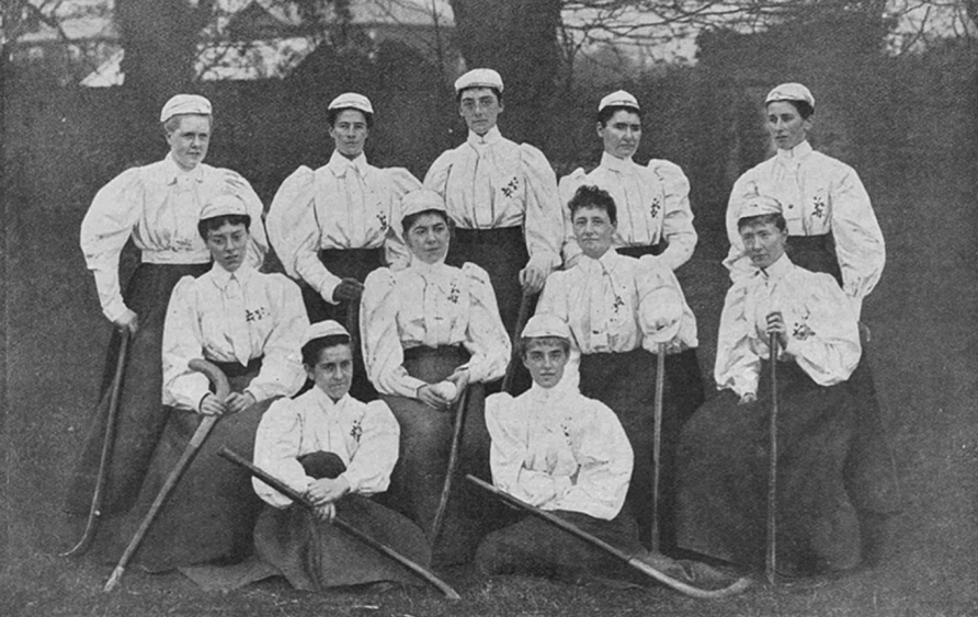 Women wearing red skirts, white bodices and caps holding hockey sticks | The Hockey Museum