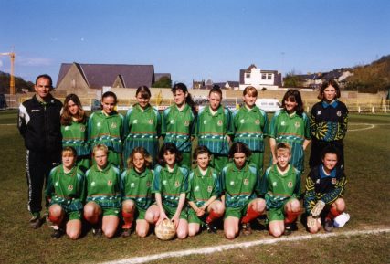 Cymru Girls team photo on pitch. Wearing Green away jersey and shorts.