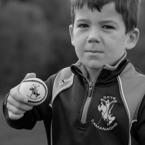 Young Boy, wearing a Skye Camanachd training top, holds a Shinty ball. In Black and White. | Isabelle Law Photography