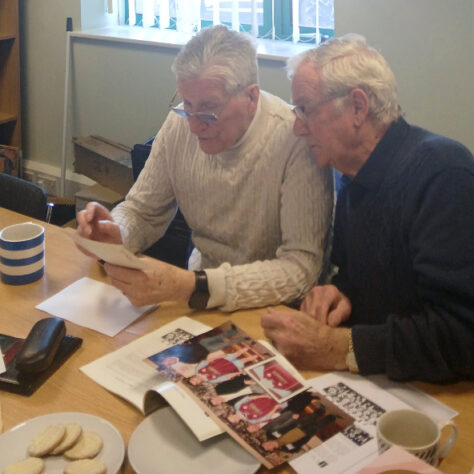 Old friends reminiscing. LIHH A group of men together looking at old photographs | Leeds Irish Health & Homes